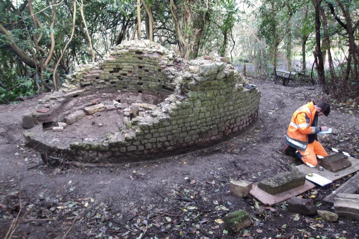 An archaeologist in high-vis kneels next to the peculiar stone structure.