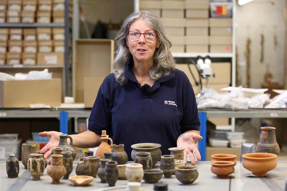 Photograph of Rachael Seager Smith, our finds manager, standing behind selection of pottery