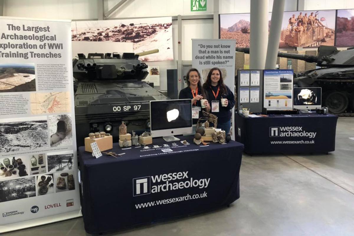 Sophie Clarke and another Wessex Archaeology STEM ambassador stand together behind table displaying finds