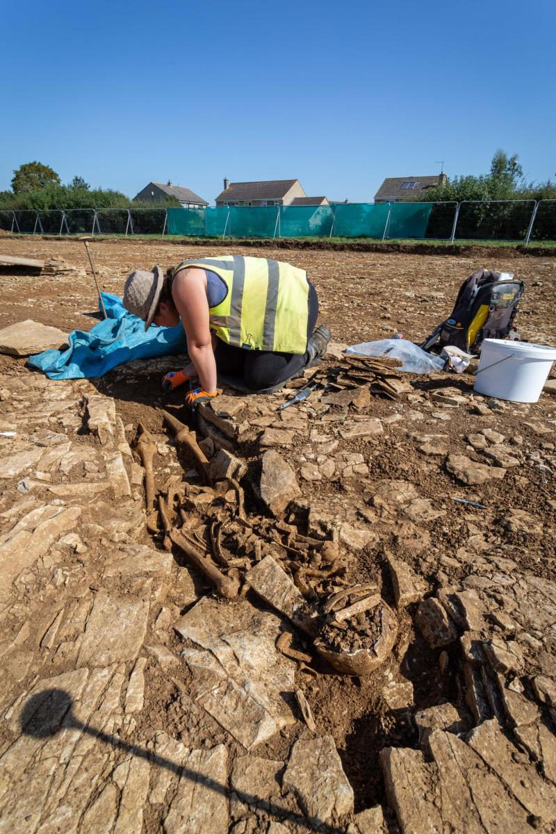 An archaeologist crouches over a skeleton which she is carefully excavating